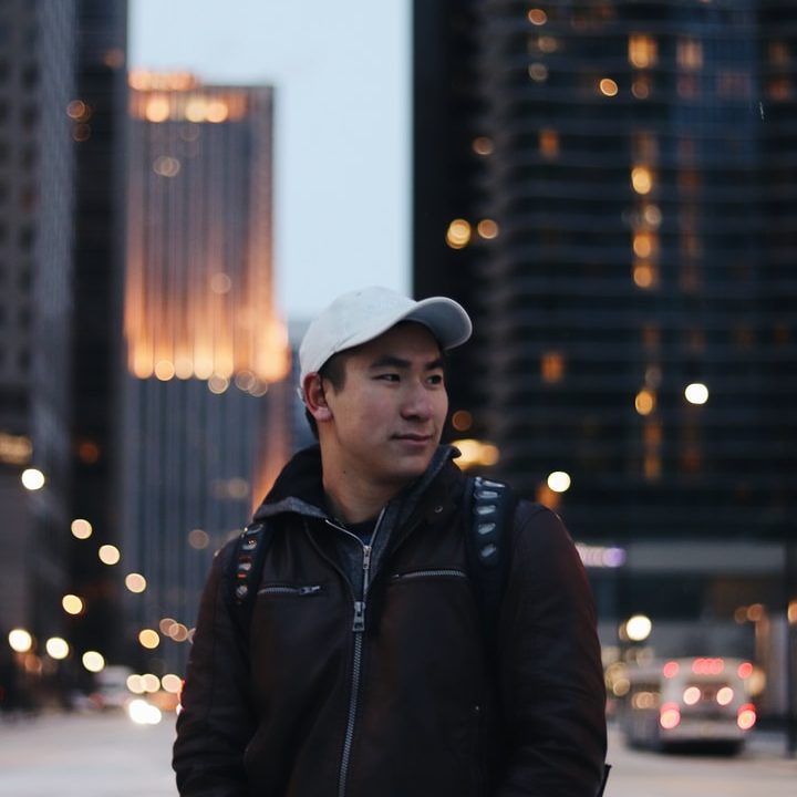 man wearing black zip-up jacket standing near high-rise building